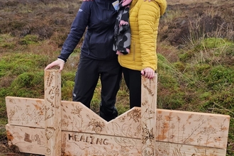 Two smiling women behind a timber dam, which is decorated with botanical artwork created by children